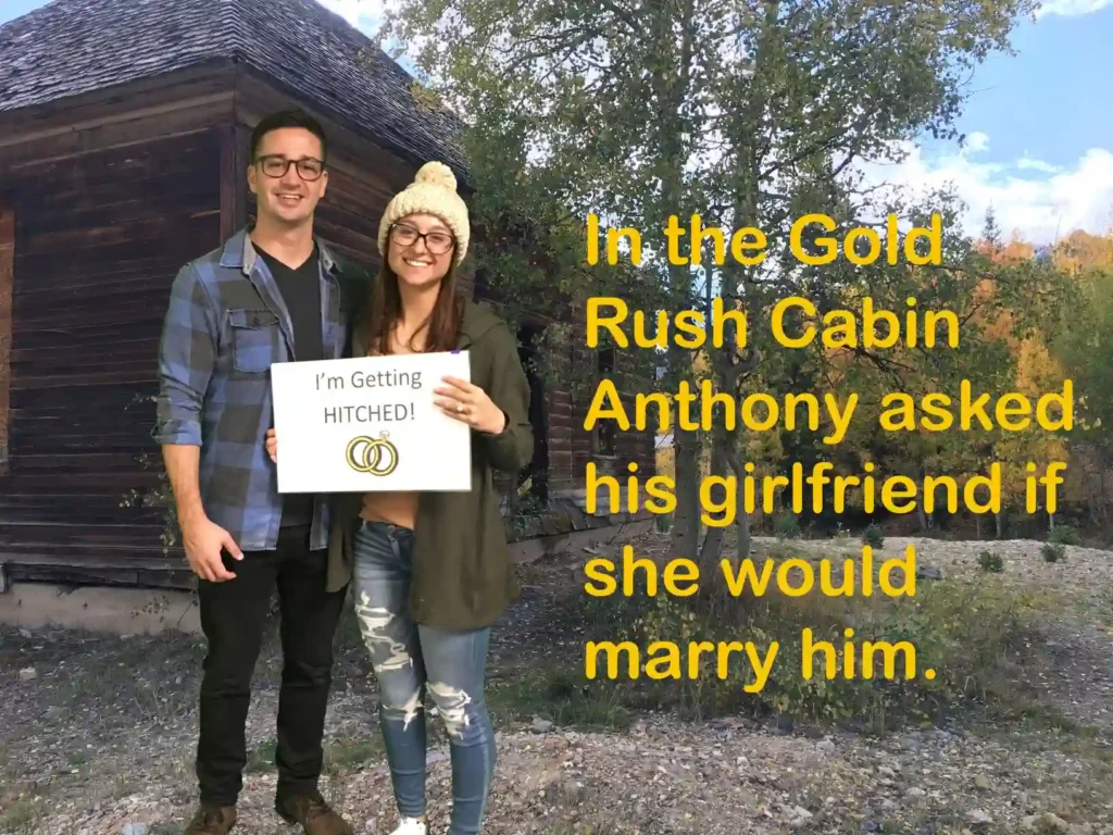 Couple standing together in front of a rustic cabin with a sign that reads 'I’m Getting Hitched!' celebrating a proposal during an escape room experience at Think in a Box, a popular double date venue in San Angelo. 